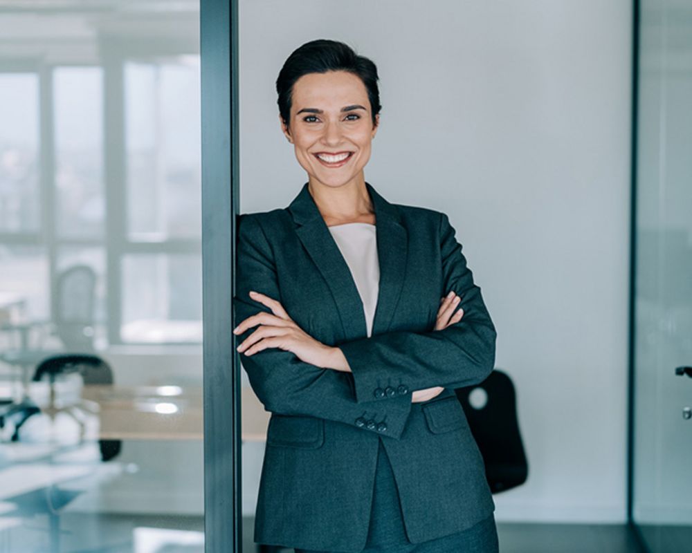 Eine weibliche Führungskraft lehnt selbstbewusst am Türrahmen ihres Büros.
