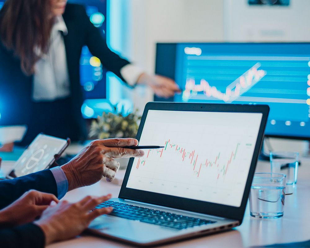 Eine Hand zeigt mit einem Stift auf den Bildschirm eines Laptops, auf dem ein Graph abgebildet ist.