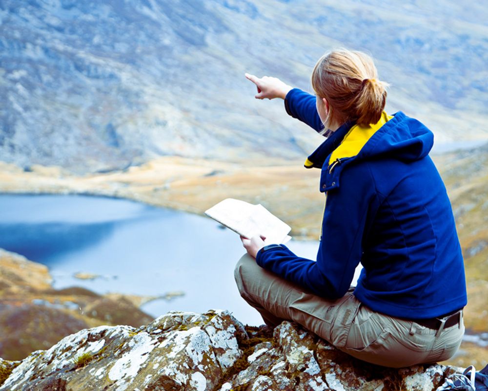 Eine Frau passiert während ihrer Wanderung in den Bergen und zeigt auf einen Berg in der Ferne.