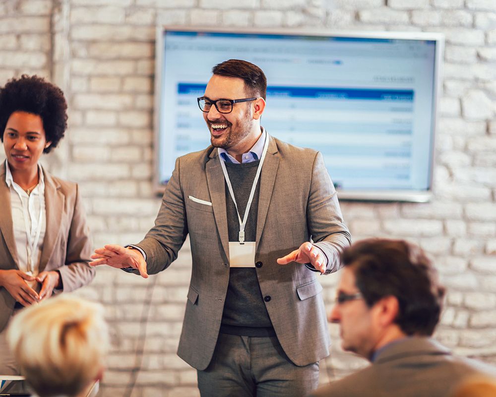 Ein Event Manager begrüßt die Teilnehmer eines Seminars vor Veranstaltungsbeginn.
