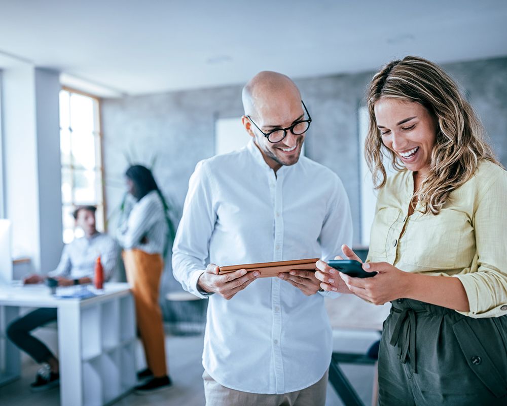 Zwei Kolleg/-innen unterhalten sich über ein Projekt der digitalen Transformation und betrachten den Projektplan auf Smartphone und Tablet.